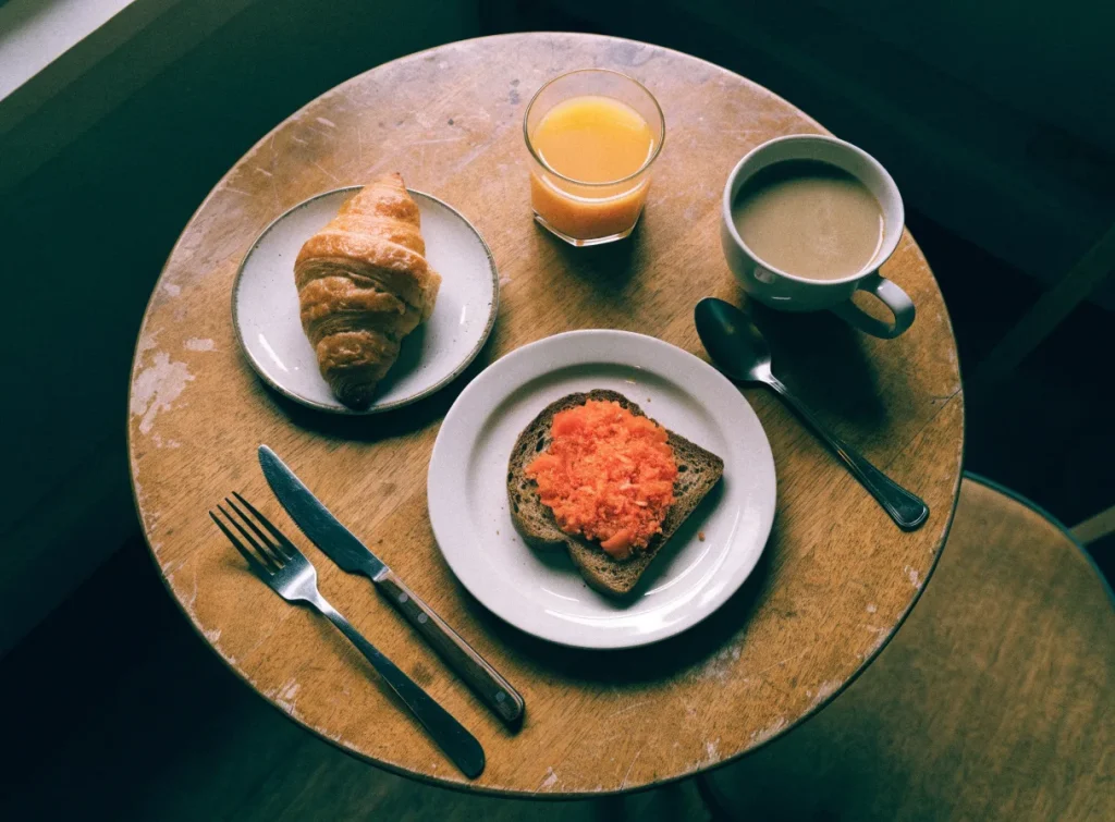 Mesa de desayuno vista desde arriba: tostada, bollería, café con leche y zumo